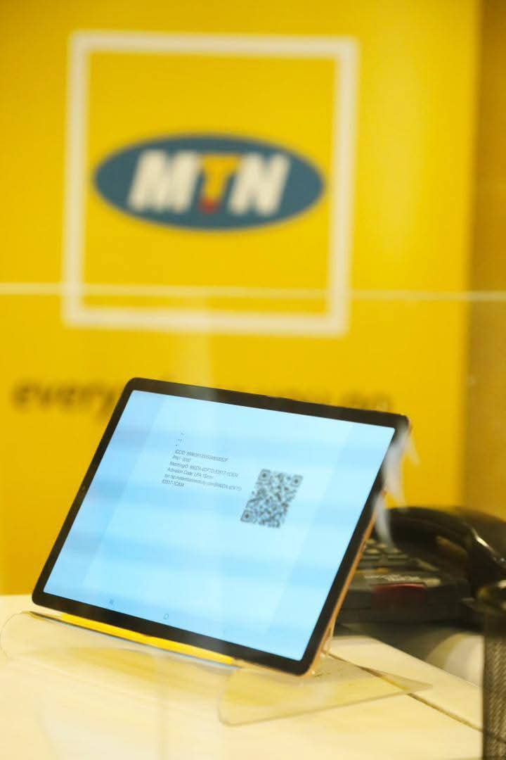 A tablet displaying a QR code, with the MTN logo in the background on a yellow backdrop.